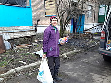 Frau steht mit einem Beutel Lebensmittel vor einem baufälligen Haus.
