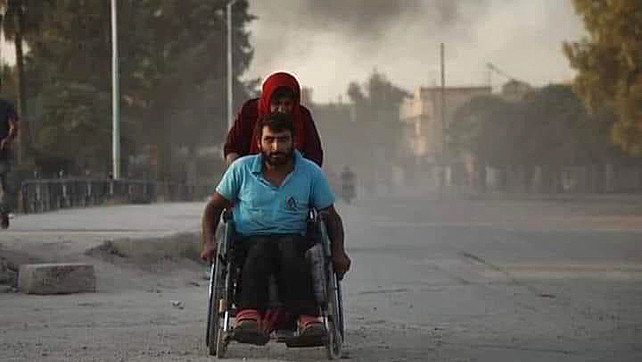 Un homme en fauteuil roulant est poussé par une femme. Les deux sont en fuite devant les coups de l'armée turque.